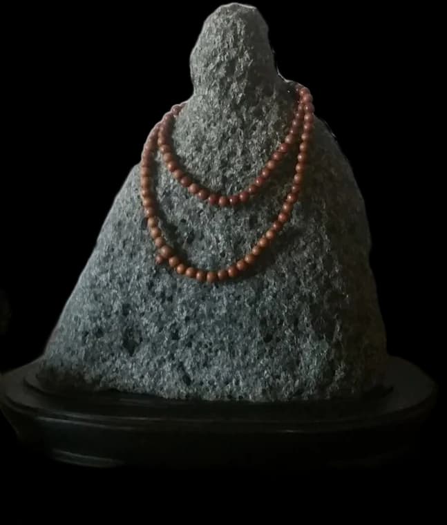 Seated Stone — a volcanic viewing stone with a wooden rosary, on a dark base